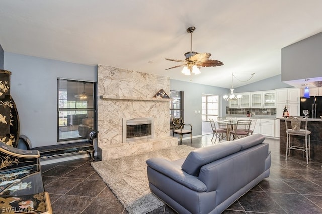 living room featuring ceiling fan, a stone fireplace, and vaulted ceiling