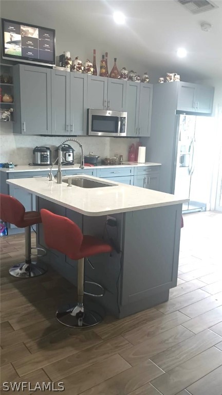 kitchen featuring tasteful backsplash, a breakfast bar, gray cabinets, and a center island with sink