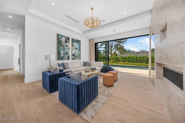 living area featuring light wood-style flooring, a notable chandelier, a fireplace, baseboards, and a raised ceiling