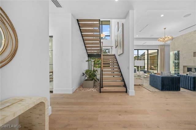 staircase featuring a fireplace, wood finished floors, visible vents, and a notable chandelier