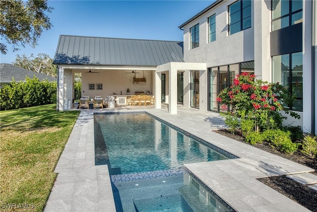 rear view of house featuring a patio, ceiling fan, a standing seam roof, a yard, and stucco siding