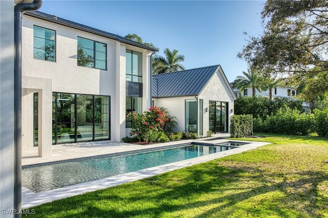 back of house featuring metal roof, a yard, an outdoor pool, a standing seam roof, and stucco siding