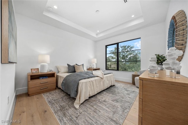 bedroom with light wood-type flooring, baseboards, and a tray ceiling