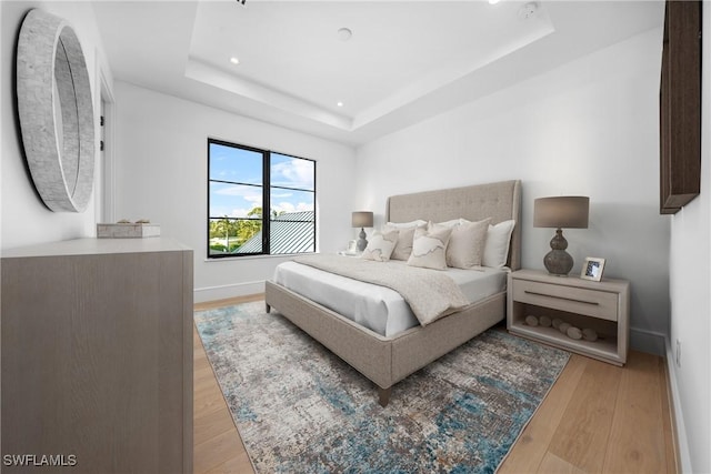 bedroom with light wood-style floors, baseboards, a raised ceiling, and recessed lighting