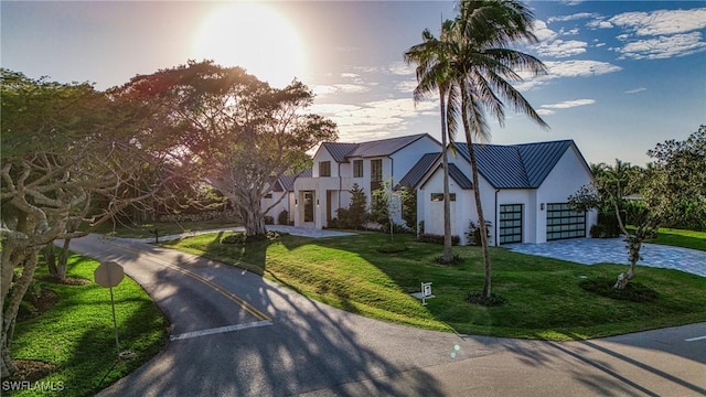 view of front facade featuring stucco siding, a standing seam roof, metal roof, driveway, and a front lawn