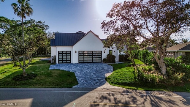 modern farmhouse style home with metal roof, a garage, decorative driveway, stucco siding, and a front yard