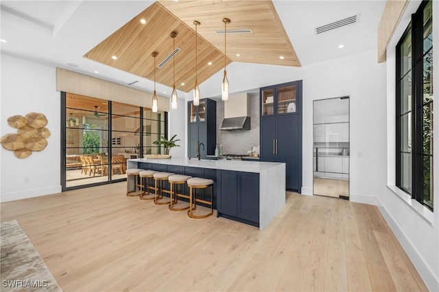 kitchen with visible vents, hanging light fixtures, light countertops, wall chimney exhaust hood, and glass insert cabinets