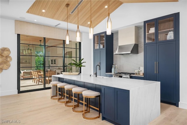 bar featuring lofted ceiling, wall chimney exhaust hood, light wood-type flooring, pendant lighting, and a sink