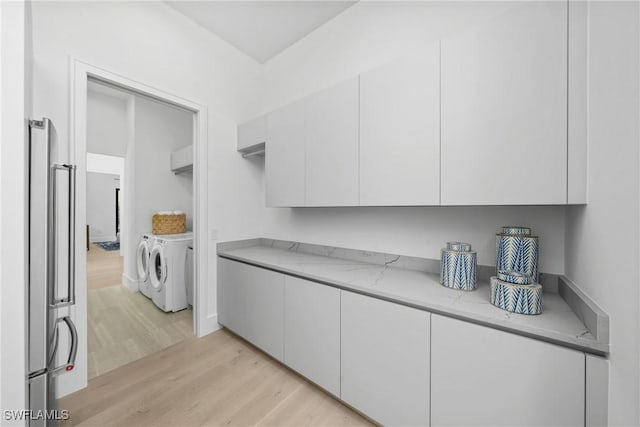 kitchen with washing machine and clothes dryer, light stone countertops, and white cabinets