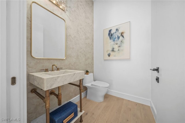 half bathroom with baseboards, toilet, and wood finished floors