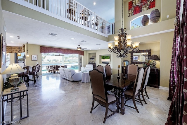 tiled dining room with ceiling fan with notable chandelier and a towering ceiling