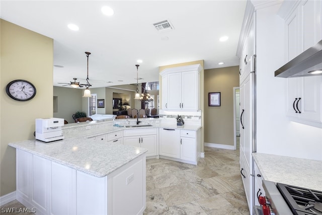 kitchen featuring light tile flooring, kitchen peninsula, ceiling fan with notable chandelier, wall chimney exhaust hood, and white cabinets