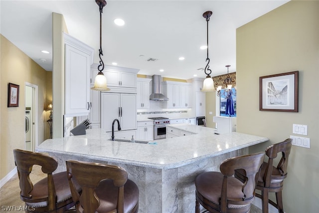 kitchen with white cabinets, decorative light fixtures, wall chimney exhaust hood, and a breakfast bar area