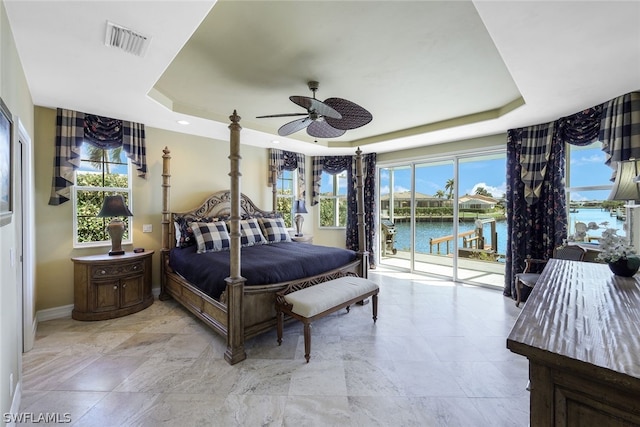 bedroom featuring a raised ceiling, a water view, light tile flooring, and ceiling fan