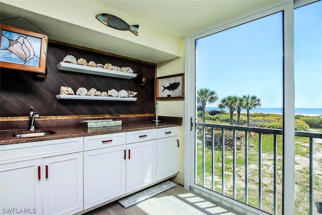 bar with a water view, dark stone counters, light hardwood / wood-style flooring, white cabinetry, and sink