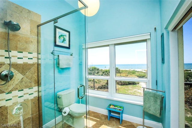 bathroom with toilet, tile flooring, a shower with shower door, and a water view