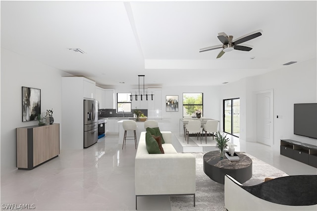 living room with ceiling fan, a tray ceiling, and sink