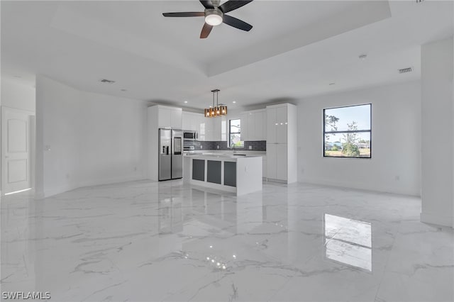 unfurnished living room featuring a raised ceiling, ceiling fan with notable chandelier, sink, and light tile floors