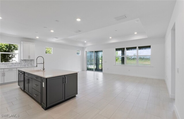 kitchen featuring plenty of natural light, white cabinetry, sink, and an island with sink