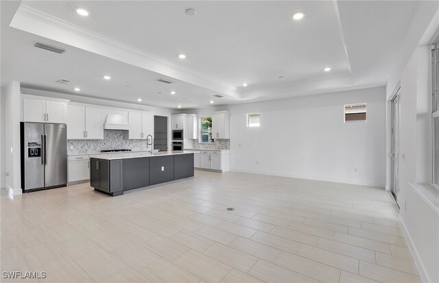 kitchen featuring a center island with sink, a raised ceiling, white cabinets, and stainless steel appliances