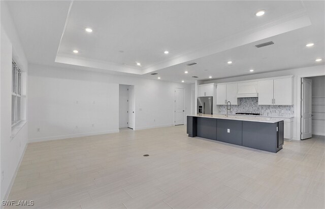 kitchen with white cabinets, a raised ceiling, a spacious island, tasteful backsplash, and high end fridge