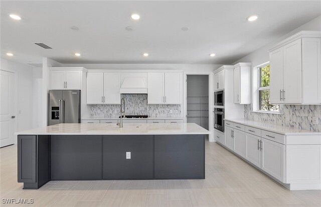 kitchen featuring white cabinets, appliances with stainless steel finishes, decorative backsplash, and a large island with sink