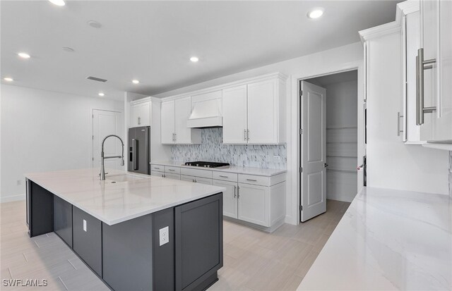 kitchen featuring light stone countertops, custom range hood, stainless steel appliances, white cabinetry, and a large island