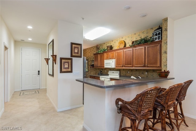 kitchen with kitchen peninsula, white appliances, backsplash, light tile flooring, and a kitchen bar