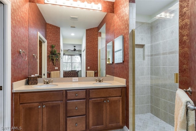 bathroom featuring tiled shower, ceiling fan, double sink, and vanity with extensive cabinet space