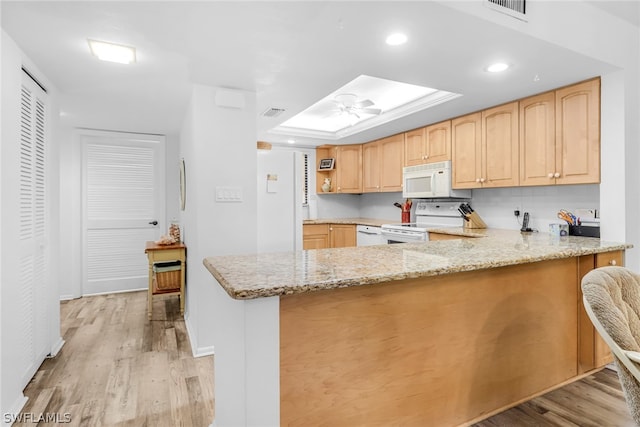 kitchen with light wood finished floors, a raised ceiling, light brown cabinetry, light stone countertops, and white appliances