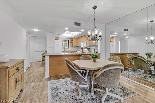 dining area featuring light wood-type flooring, a skylight, and an inviting chandelier