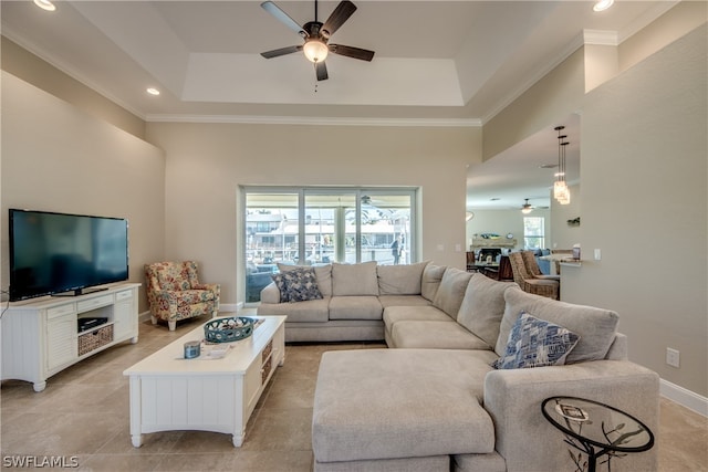 tiled living room featuring a raised ceiling, ornamental molding, and ceiling fan