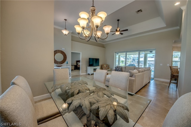 dining space with light tile flooring, ornamental molding, ceiling fan with notable chandelier, and a tray ceiling