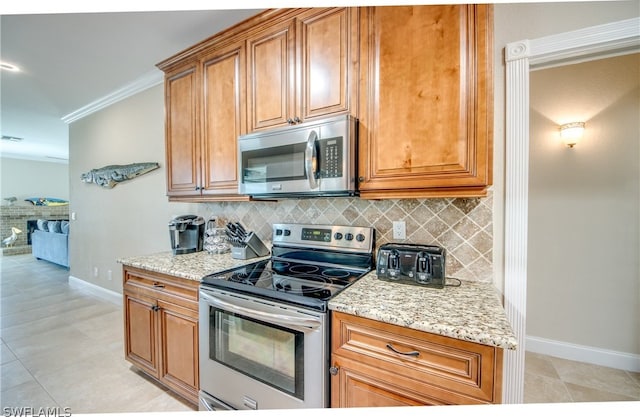 kitchen featuring ornamental molding, appliances with stainless steel finishes, light tile flooring, light stone countertops, and tasteful backsplash