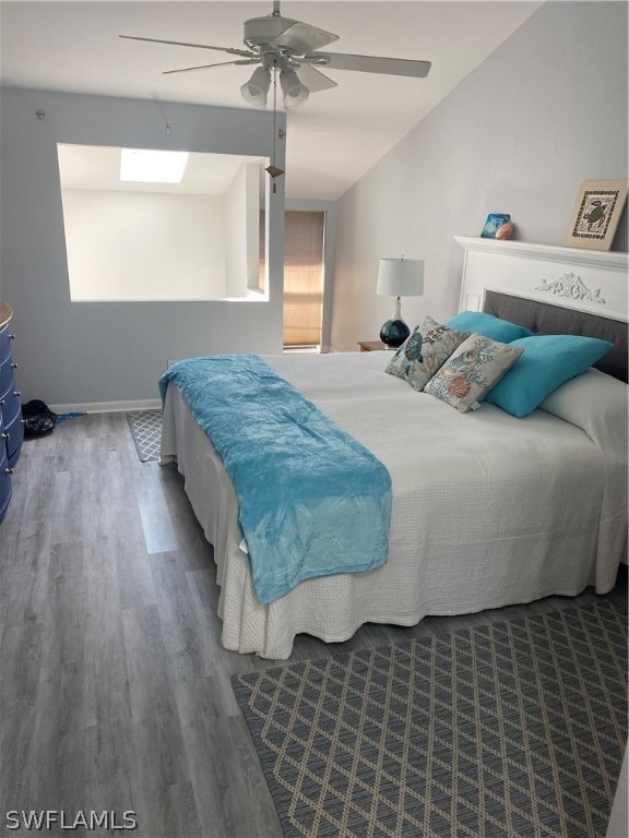 bedroom featuring vaulted ceiling with skylight, dark wood-type flooring, and ceiling fan