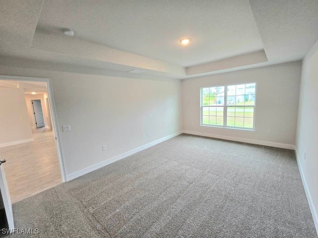 spare room with a tray ceiling, light colored carpet, and a textured ceiling