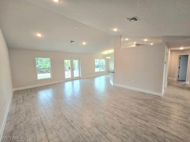 empty room with lofted ceiling, a textured ceiling, and french doors