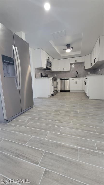 kitchen featuring appliances with stainless steel finishes, sink, backsplash, white cabinetry, and a tray ceiling