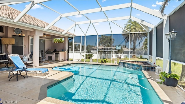 view of swimming pool with a patio area, ceiling fan, glass enclosure, and an outdoor kitchen