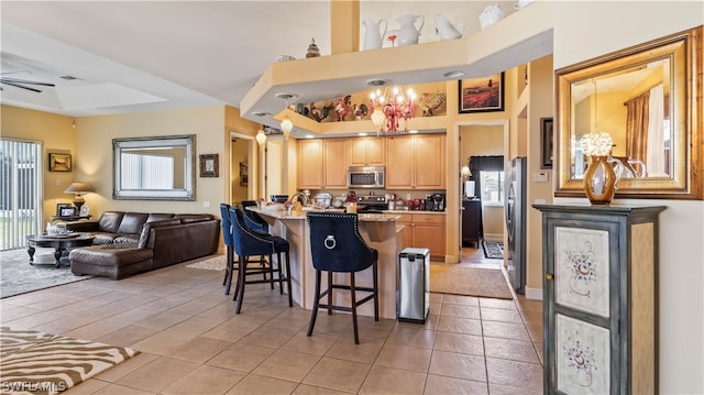 kitchen featuring a kitchen breakfast bar, light tile patterned floors, stainless steel appliances, and ceiling fan with notable chandelier