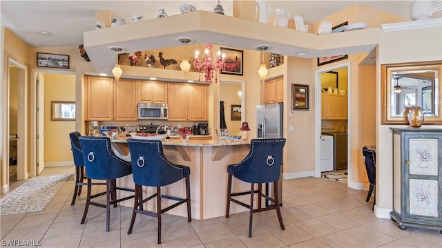 kitchen featuring appliances with stainless steel finishes, light stone counters, a breakfast bar, light tile patterned floors, and washer / clothes dryer