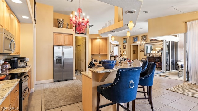 kitchen with a breakfast bar, light stone countertops, stainless steel appliances, and an inviting chandelier