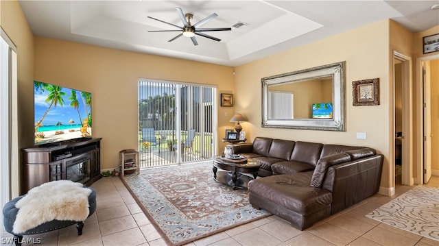 tiled living room with a raised ceiling and ceiling fan