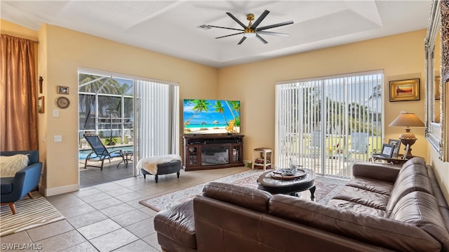 tiled living room with a tray ceiling and ceiling fan