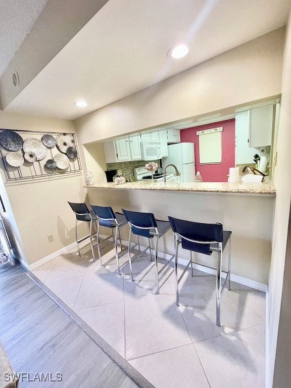 kitchen with a kitchen bar, white appliances, kitchen peninsula, and light tile patterned floors