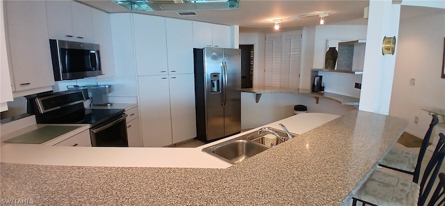 kitchen featuring a kitchen bar, kitchen peninsula, sink, white cabinetry, and appliances with stainless steel finishes