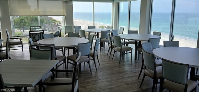 dining space with dark wood-type flooring, a beach view, and a water view