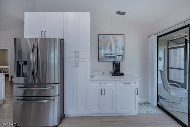 kitchen featuring white cabinets, stainless steel fridge with ice dispenser, and vaulted ceiling