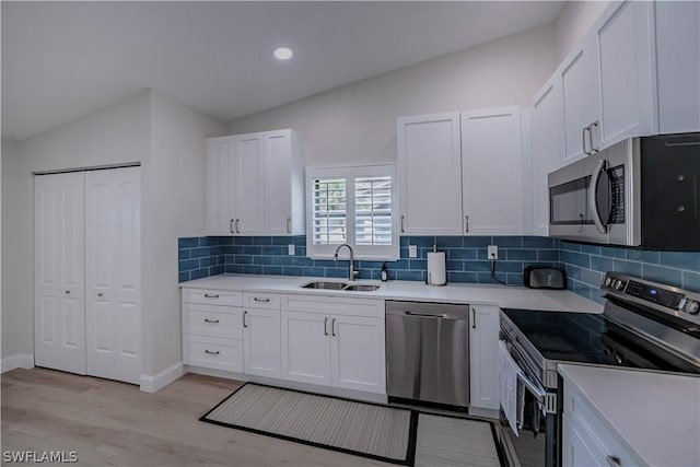 kitchen featuring vaulted ceiling, stainless steel appliances, light wood-type flooring, white cabinetry, and sink