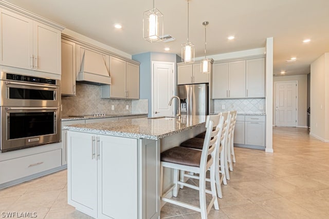 kitchen with hanging light fixtures, appliances with stainless steel finishes, sink, custom range hood, and tasteful backsplash